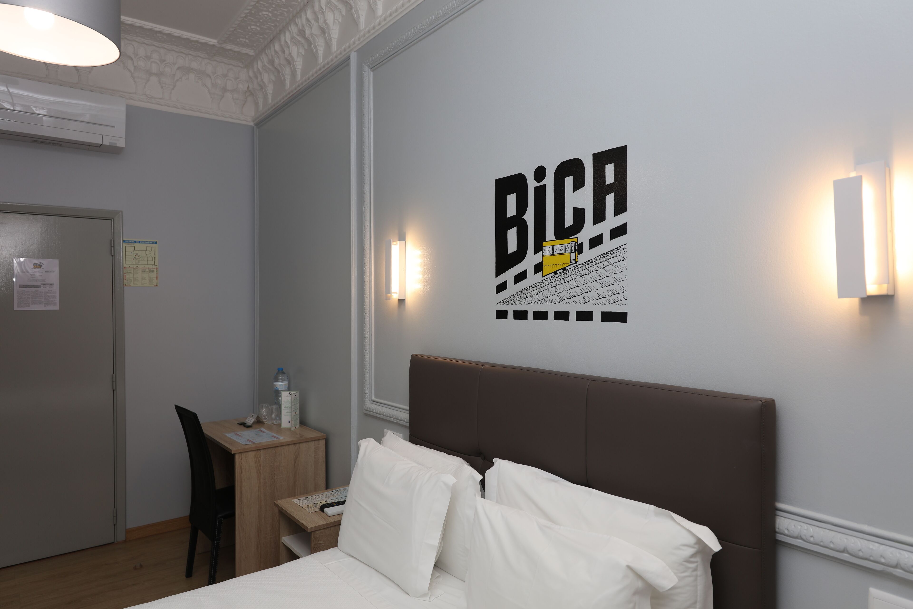 Een hotelkamer met een bed, een bureau, een stoel en een wandlamp.