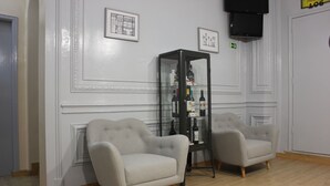 A room with two grey armchairs, a glass display cabinet with bottles, and a television mounted on the wall. - O Elétrico Guesthouse (Lisbon)