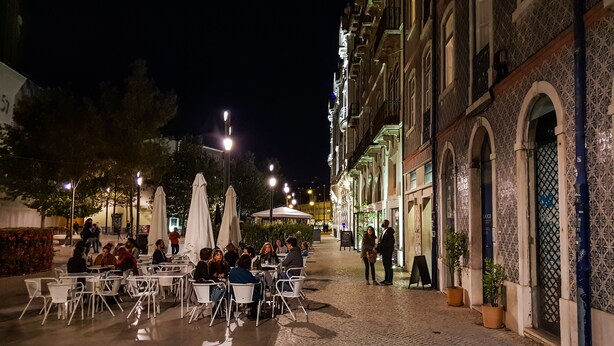 An outdoor café with tables and chairs, a cobblestone path, and buildings with ornate facades. - O Elétrico Guesthouse (Lisbon)