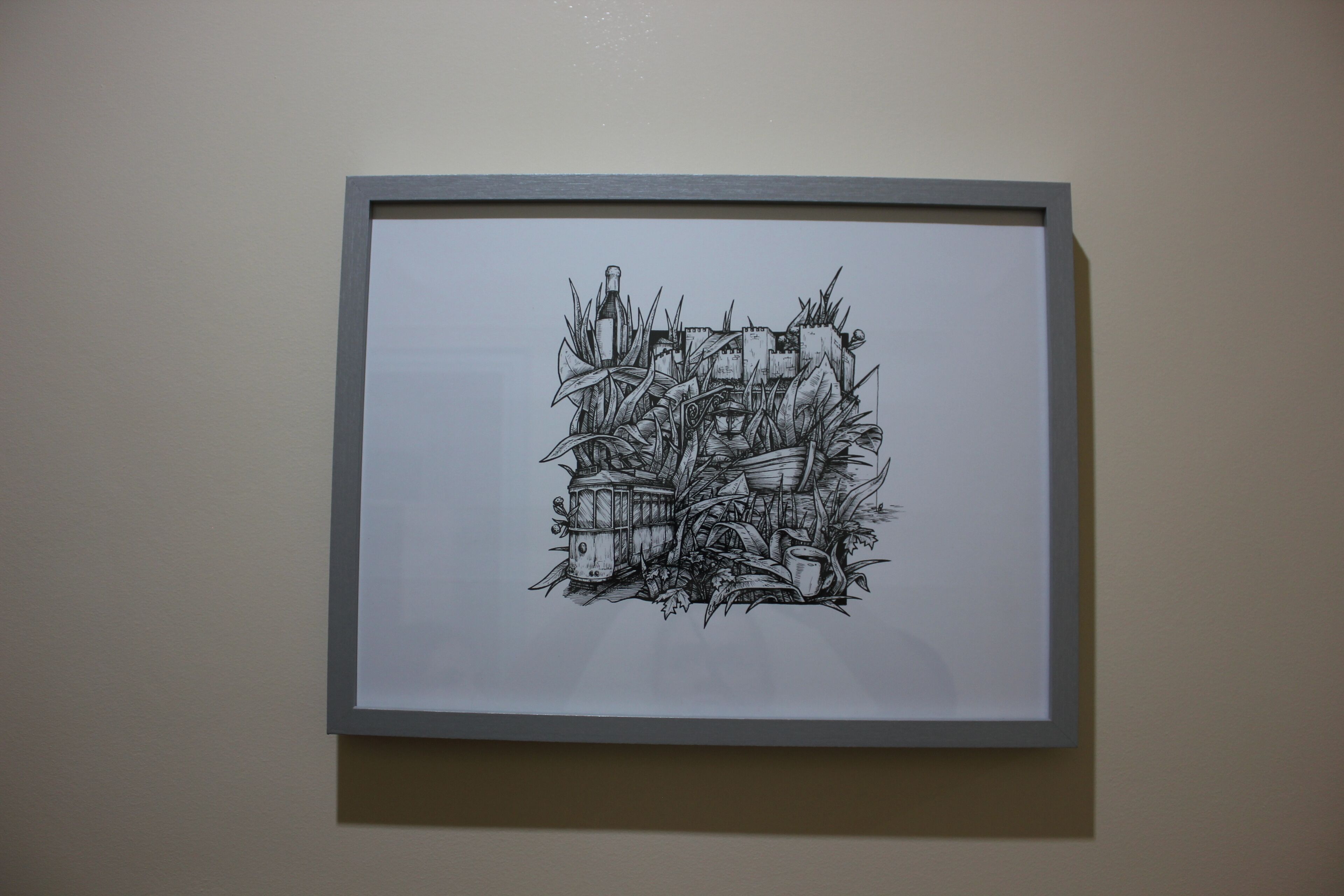 A framed black and white drawing of a castle surrounded by foliage and a bottle.