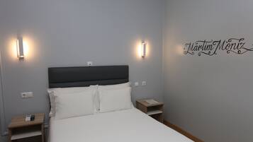 A neatly made bed with white linens and two bedside tables, one with a phone and the other with a lamp.