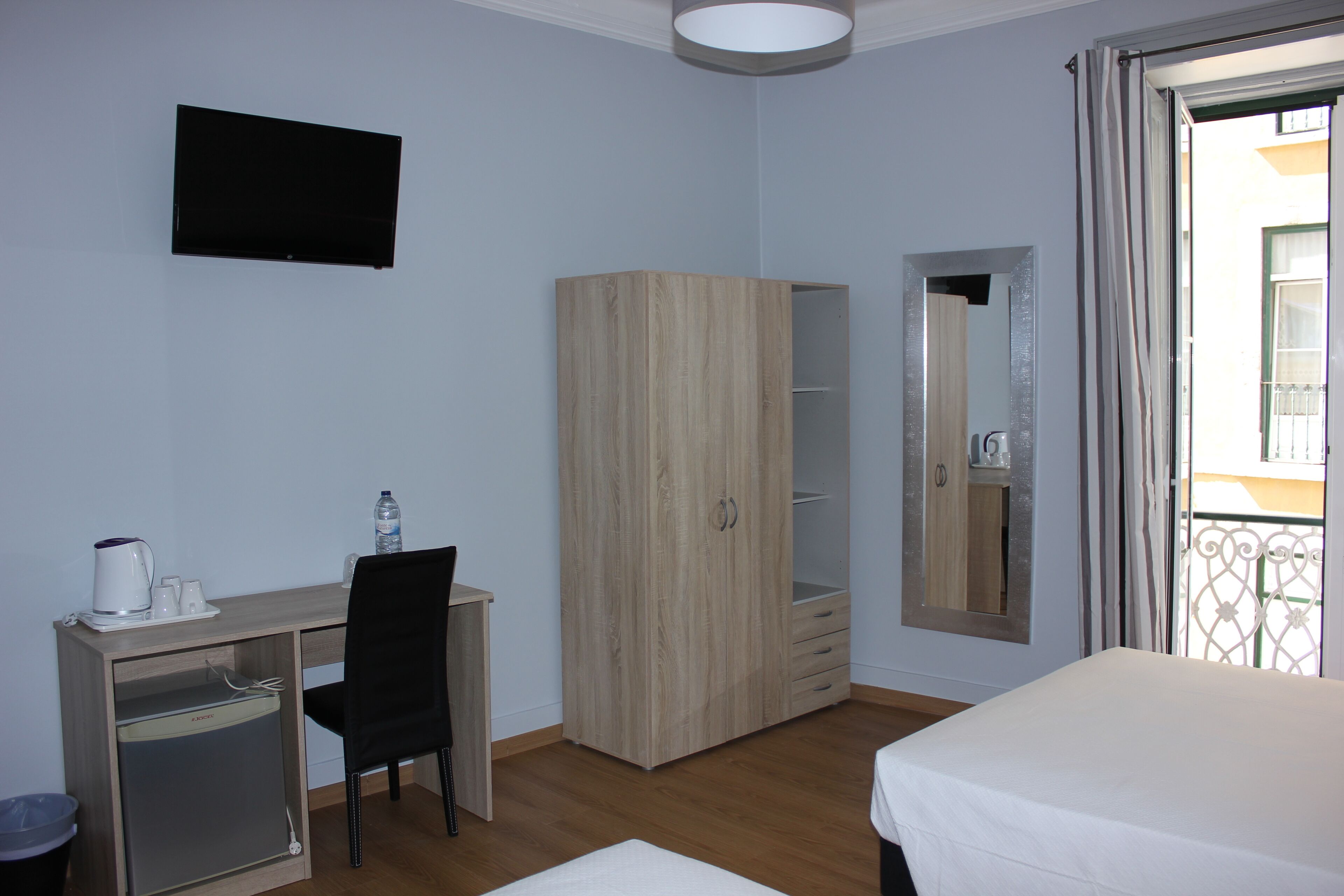 A hotel room with a desk, chair, wardrobe, bed, and a television.