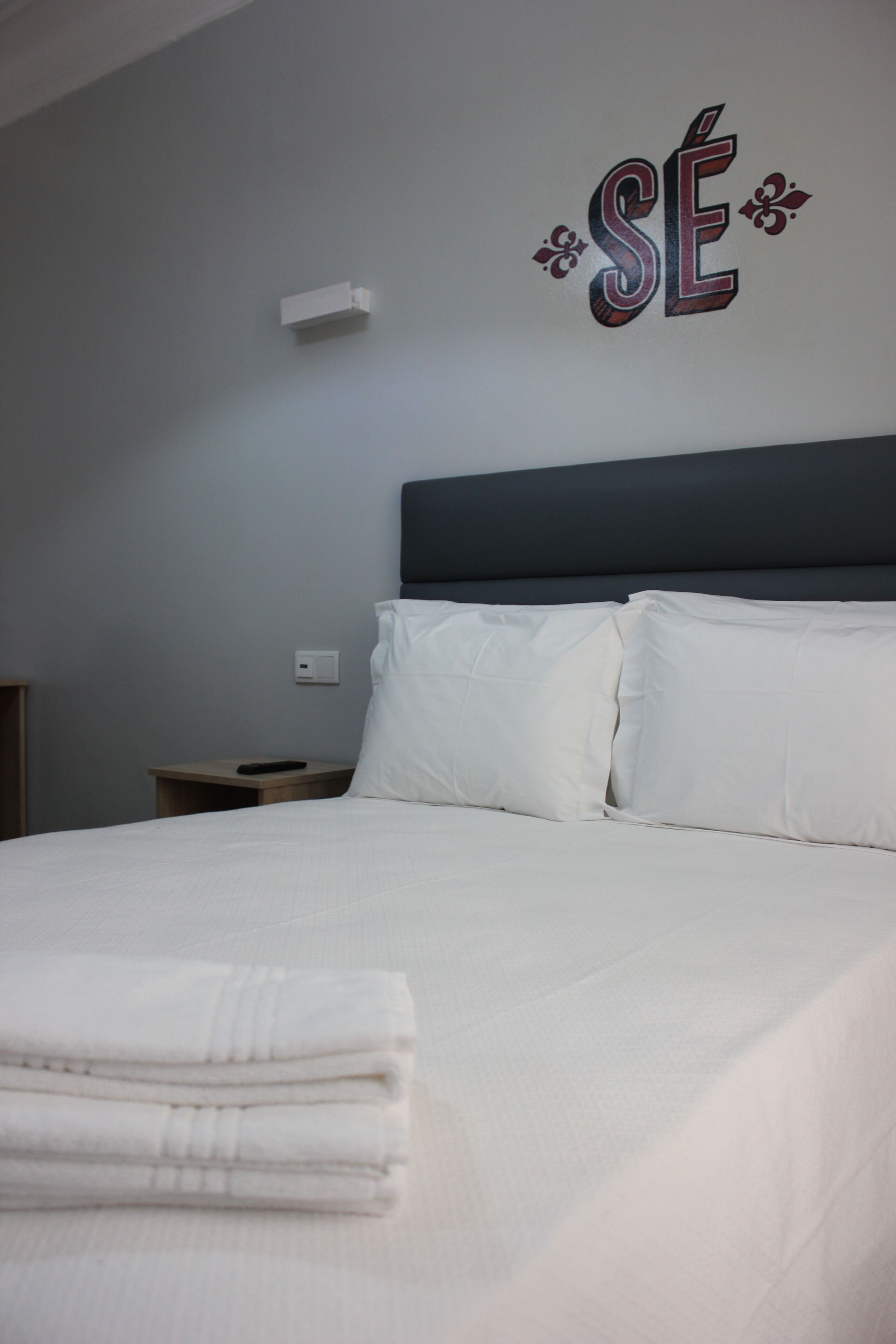 Ein ordentlich gemachtes Bett mit weißen Leinentüchern und einem gefalteten Handtuch am Fußende.