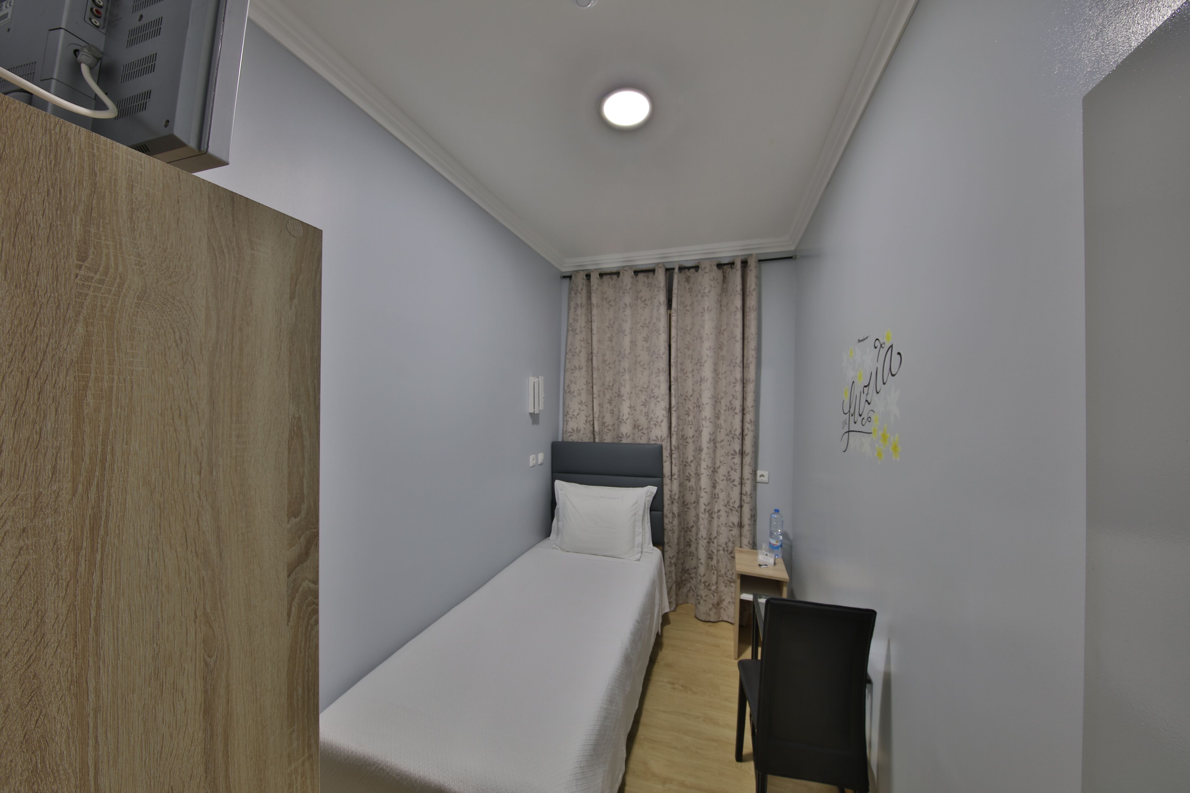 A small, neatly arranged room with a single bed, a desk, and a chair.
