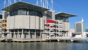 A waterfront building with a modern architectural design, featuring a prominent central structure with a flat roof and multiple levels. - O Elétrico Guesthouse (Lisbon)