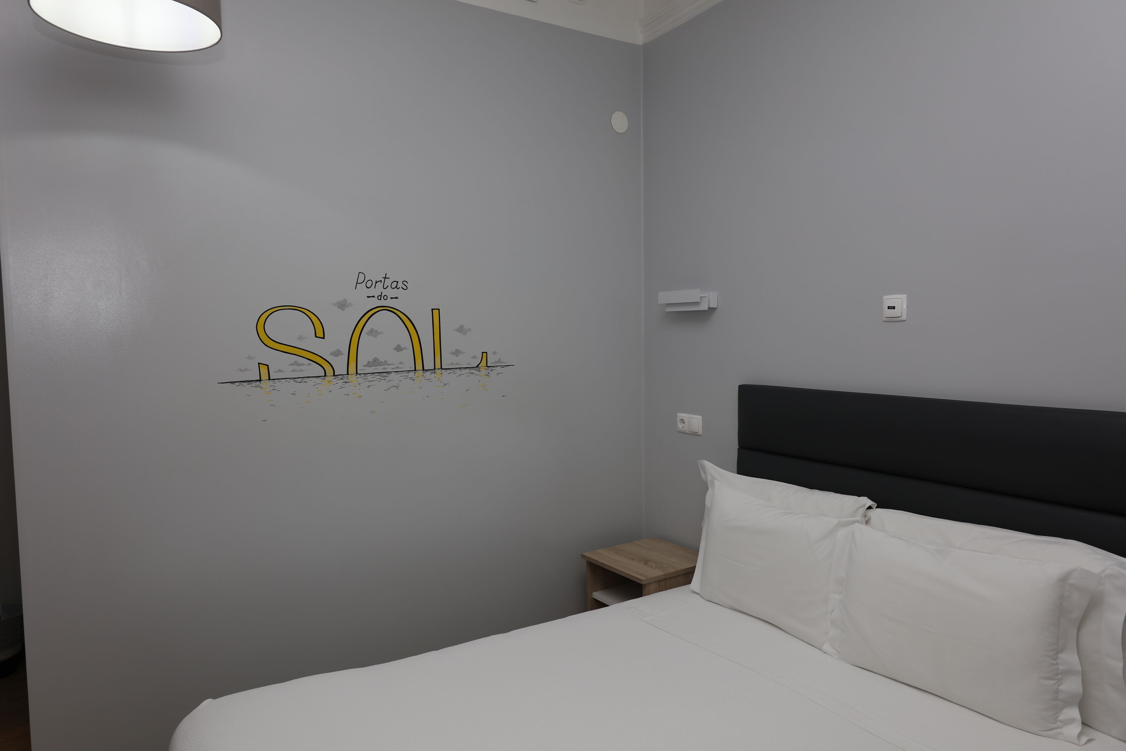 A hotel room with a bed, a nightstand, a wall with a decorative sign, and a ceiling light.