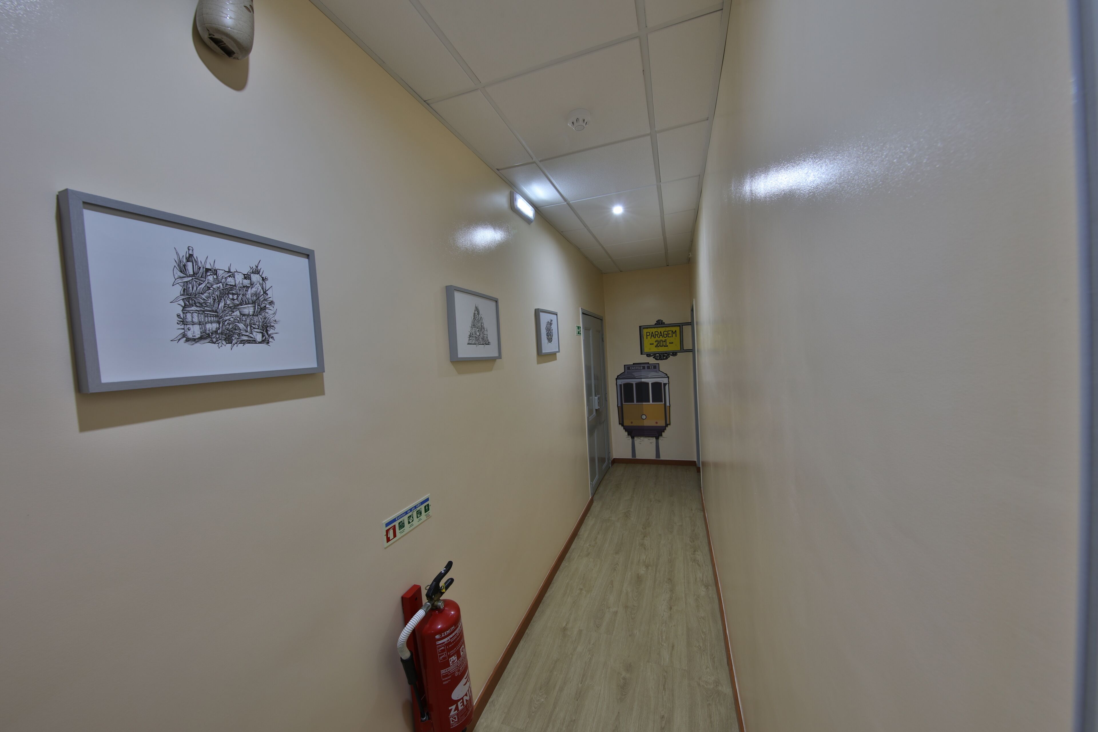 A hallway with framed artwork on the walls, a fire extinguisher, and a sign indicating the direction to the parking area.
