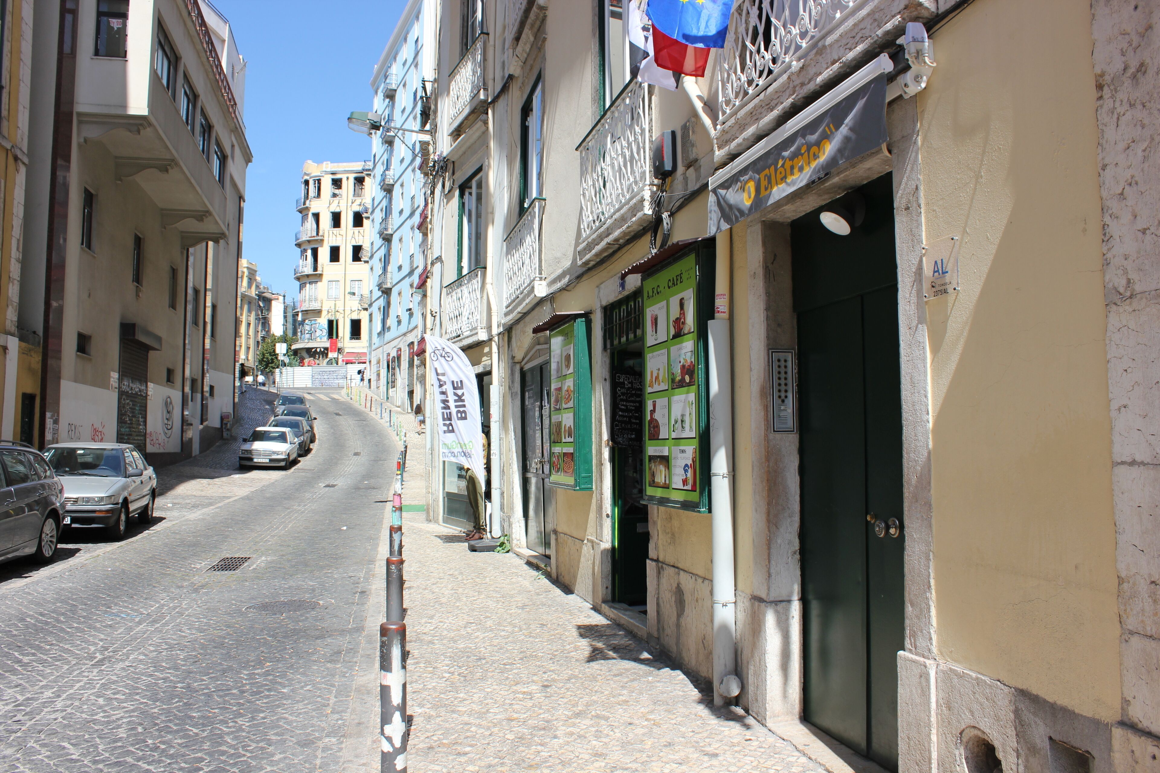 Una estrecha calle adoquinada flanqueada por edificios de varios pisos, algunos con balcones y carteles que indican negocios locales.