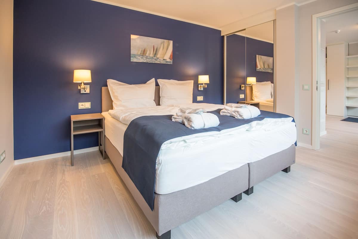 Ett modernt hotellrum med en stor säng, sänglampor, ett nattduksbord och en spegel.
