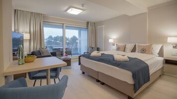 Una habitación de hotel con una cama grande, un escritorio, una silla y una ventana con vistas a árboles.