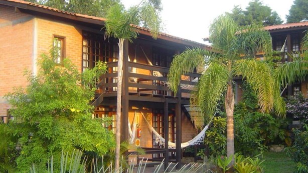 A two-story building with a wooden balcony and a hammock. - Pousada Além do Jardim (Imbituba)