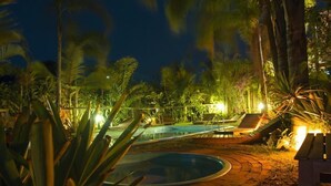 A nighttime pool area with lounge chairs and a small deck. - Pousada Além do Jardim (Imbituba)