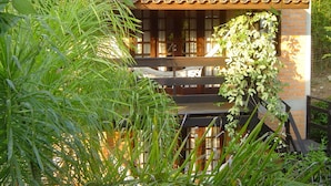 A small, rustic building with a tiled roof, a wooden bench, and lush greenery. - Pousada Além do Jardim (Imbituba)