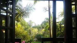 An open doorway leading to a lush garden with various plants and a wooden fence. - Pousada Além do Jardim (Imbituba)