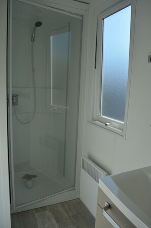 A glass-enclosed shower with a handheld showerhead, a small window above the shower, and a white sink with a countertop. - Camping de Nevers (Nevers)