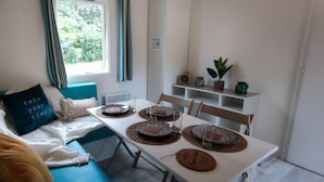 A cozy room with a teal sofa, a white table set for dining, and a window with curtains. - Camping de Nevers (Nevers)