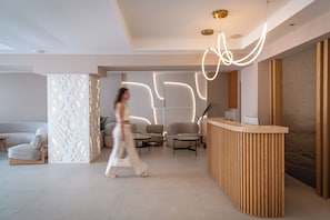 A modern reception area with a wooden reception desk, seating area with sofas and chairs, and a decorative light installation. - Mary Hotel & Mary Royal Suites (Rethymno)