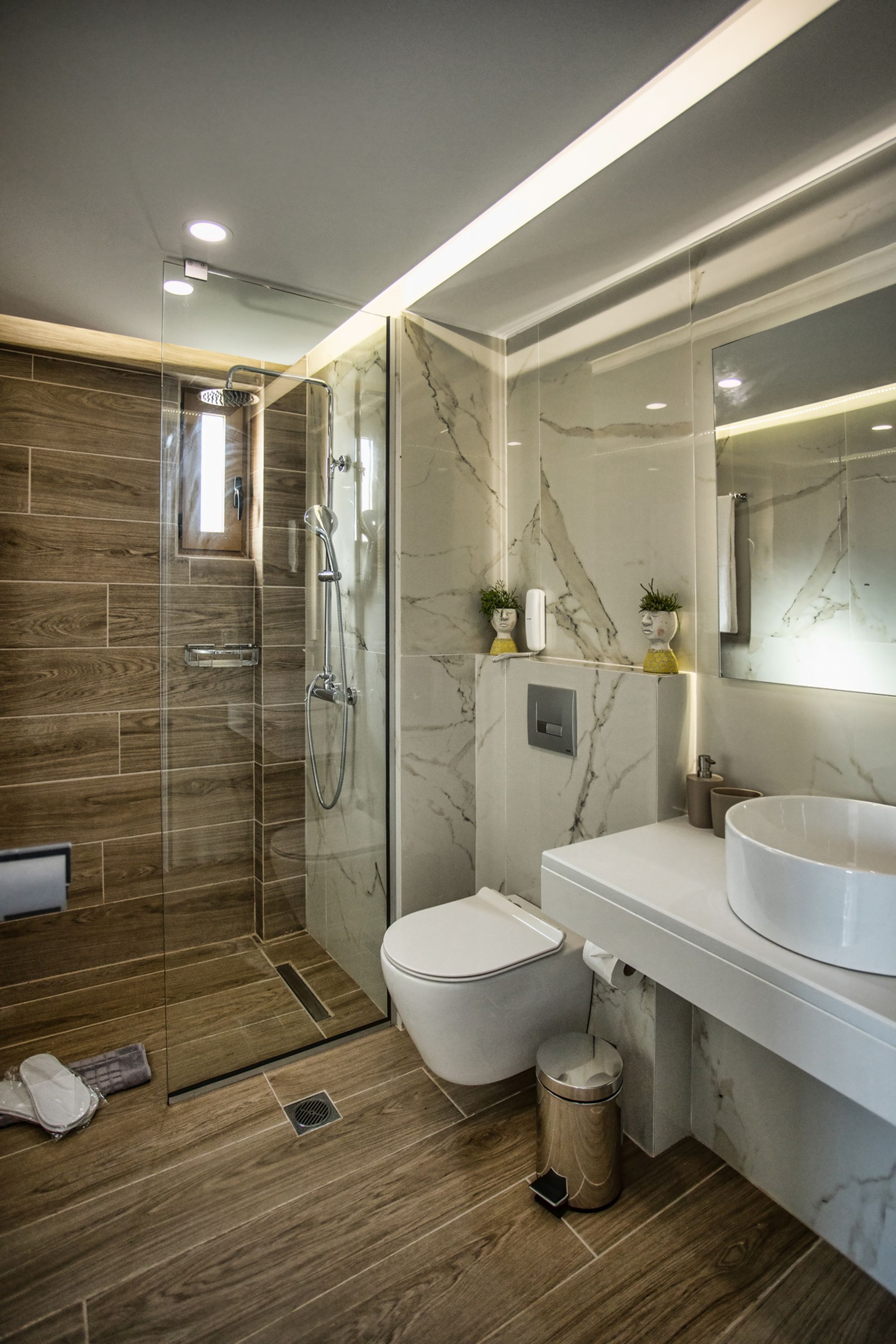 Een moderne badkamer met een douchecabine van glas, een wit toilet en een groot wastafelmeubel met een marmeren blad.