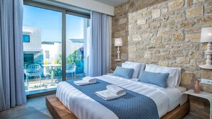 Une chambre d’hôtel moderne avec un grand lit, un mur en pierre et un balcon agrémenté d’une table et de chaises.