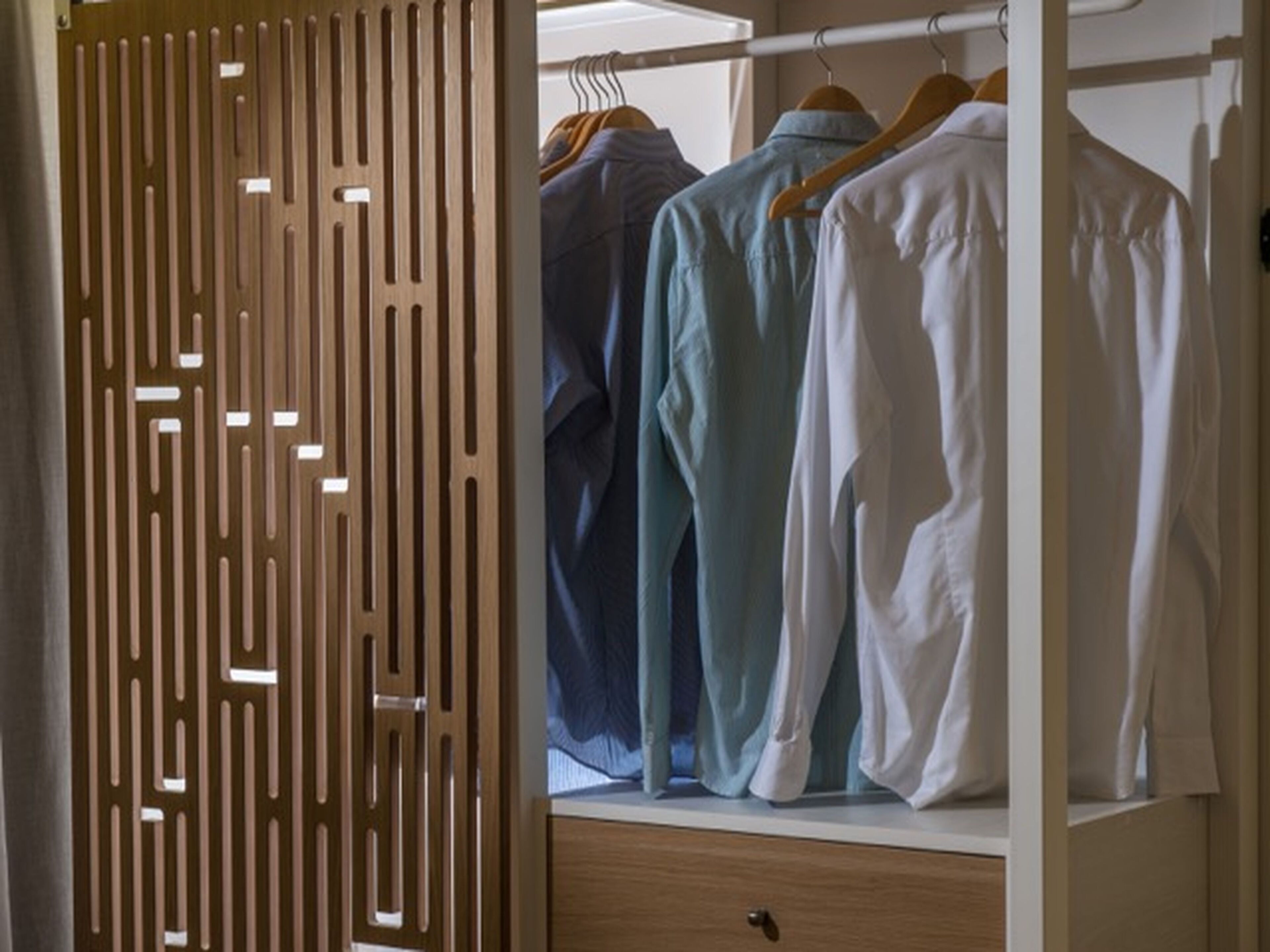 Un armario de madera con un diseño geométrico, que contiene ropa colgada y un cajón de madera.