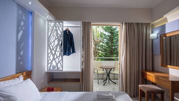 A hotel room with a bed, a desk, a chair, a small table, and a balcony with a view of trees.