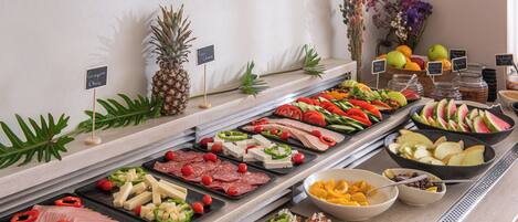 Een buffet met diverse etenswaren, waaronder vlees, kaas, fruit en groenten.