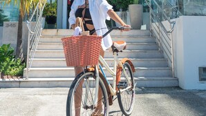 Eine Frau auf einem Fahrrad vor dem Hotel Praia Bonita, neben ihr ein Korb und eine Pflanze.