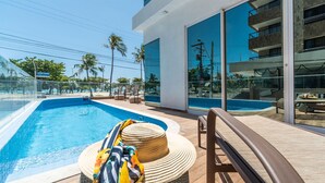Ein modernes Hotel mit großem Pool, Sitzgelegenheiten im Freien und Blick auf den Strand.