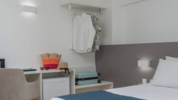 Habitación de hotel con cama, escritorio, silla, maleta y ropa colgada.