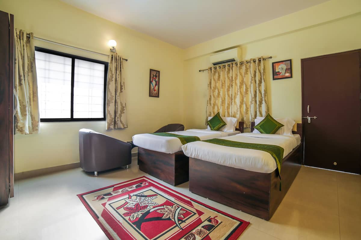 A hotel room with two beds, a chair, a window with curtains, a door, and a wall-mounted air conditioner.