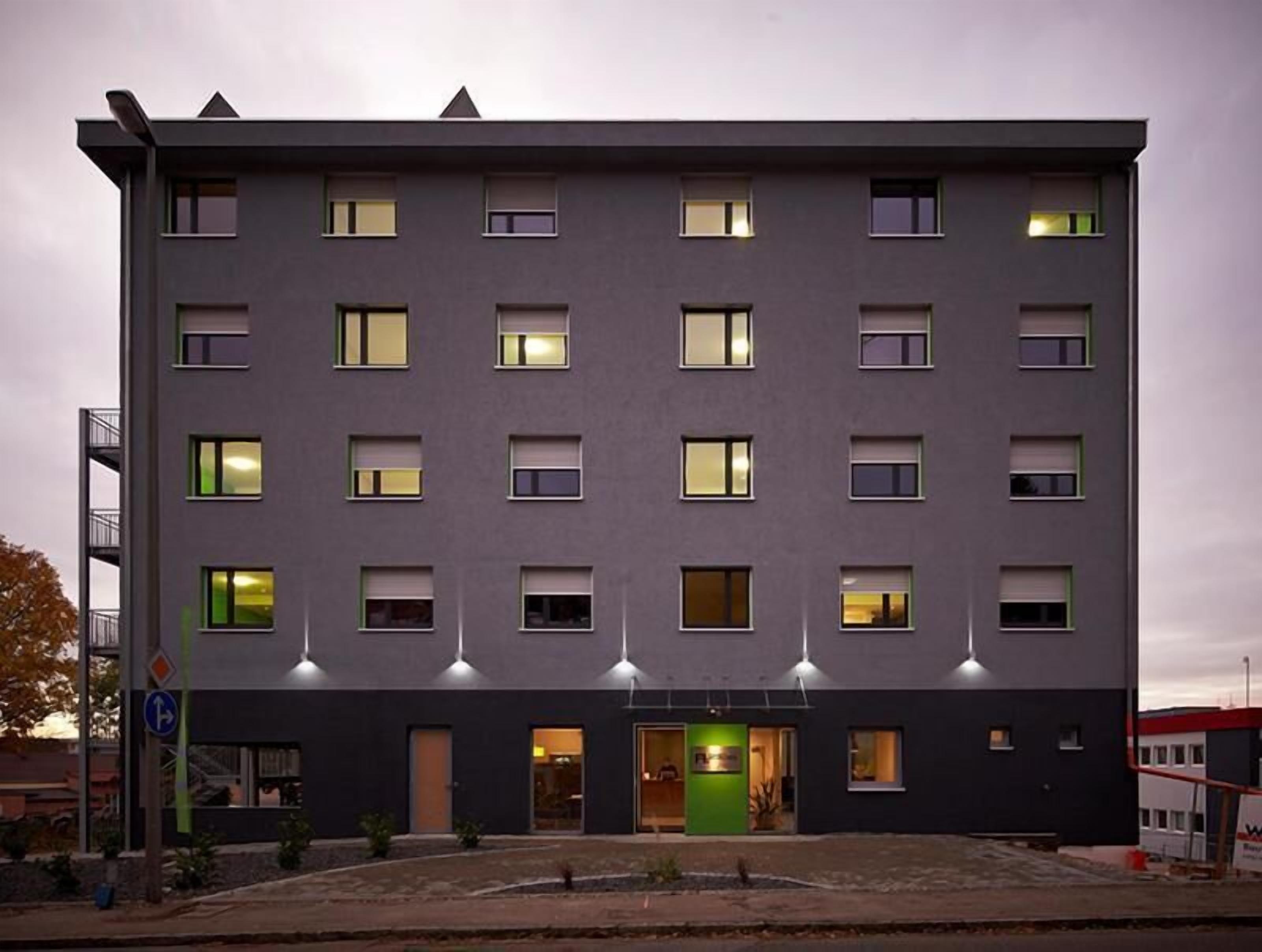 A modern multi-story building with a flat roof, evenly spaced windows, and a central entrance with a green door.