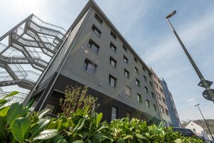 Um edifício moderno com vários andares, apresentando uma estrutura de escadas notável à esquerda e uma série de janelas na fachada.