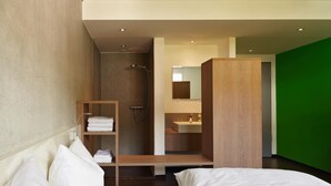 A modern hotel room with a bed, a wooden shelf with towels, a shower area, and a green accent wall. - a2 HOTELS Plochingen (Plochingen)