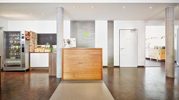 A modern reception area with a wooden reception desk, a vending machine, and a wall with text. - a2 HOTELS Plochingen (Plochingen)
