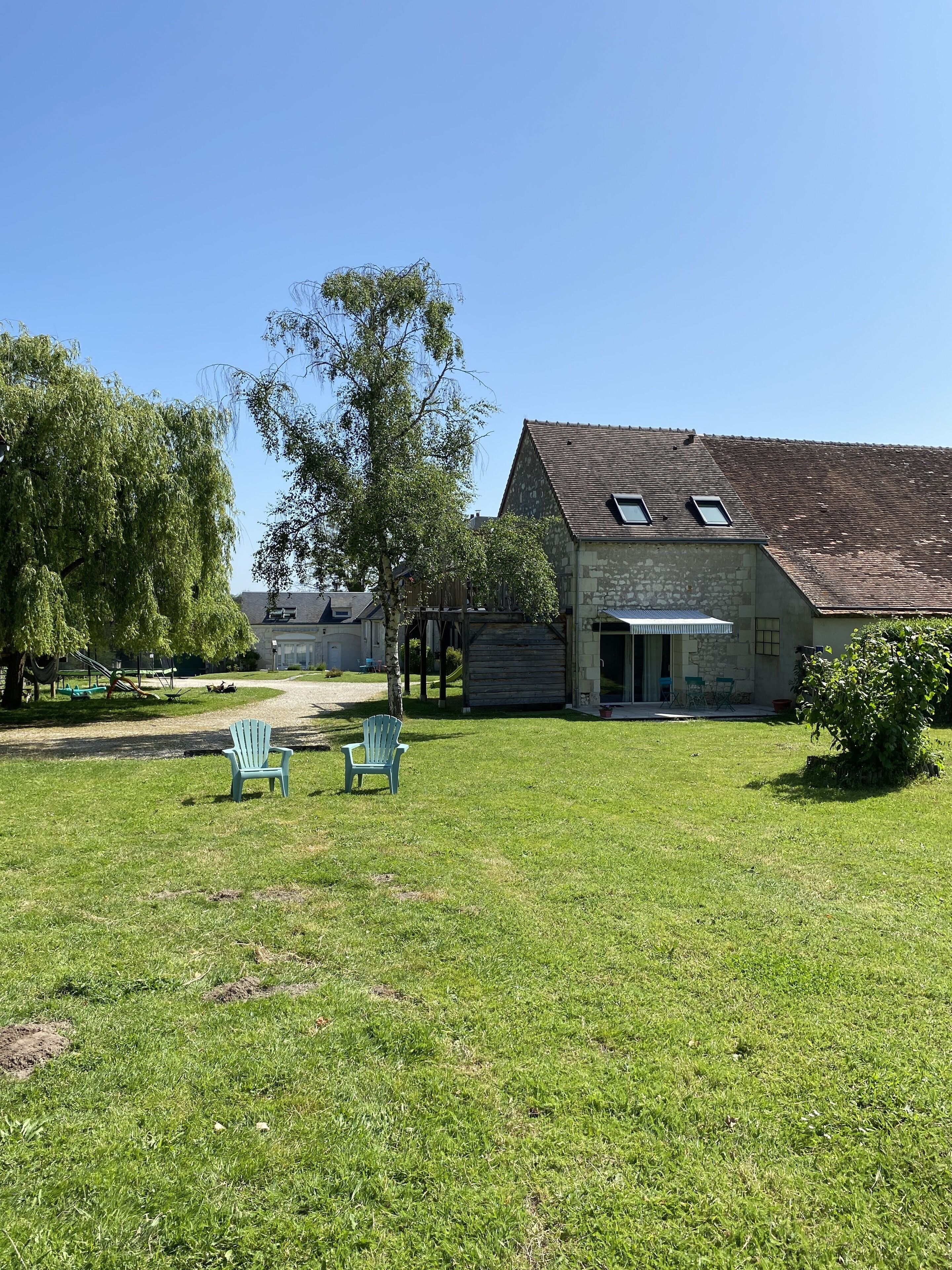 A stone building with a sloped roof and skylights, a grassy yard with two blue chairs, and a tree in the background.