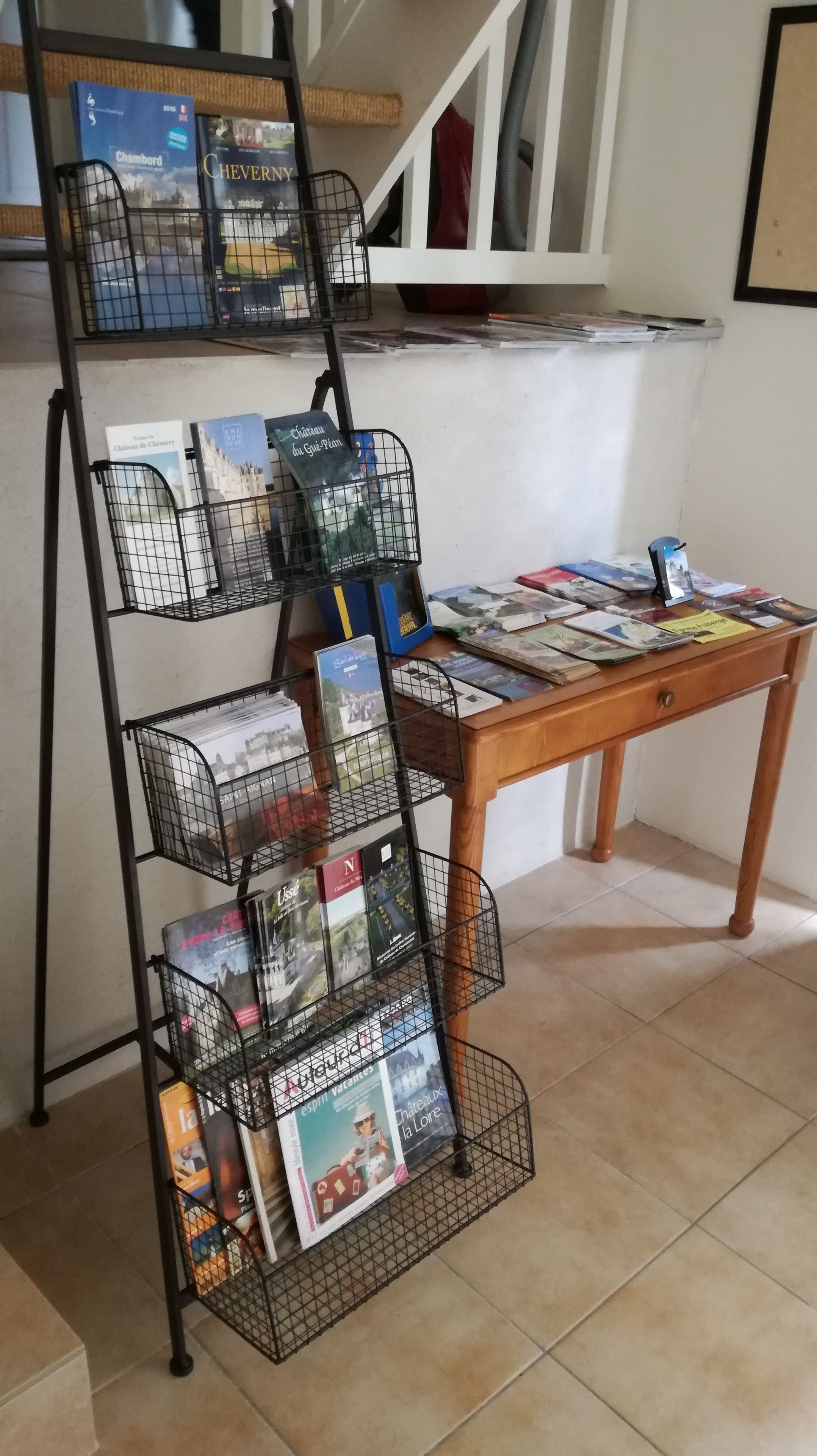 A black metal book rack with multiple shelves holding travel brochures and magazines.