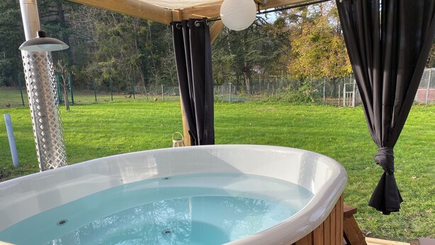 Un bain à remous doté d’une terrasse en bois, entouré d’une clôture en bois et d’arbres.