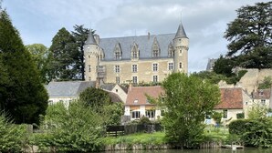 Un bâtiment historique doté d’un fossé, entouré d’arbres et bordé d’une étendue d’eau paisible.