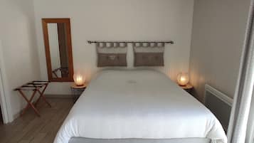 A bedroom with a large bed, two bedside lamps, a wooden chair, a mirror, and a window with curtains.
