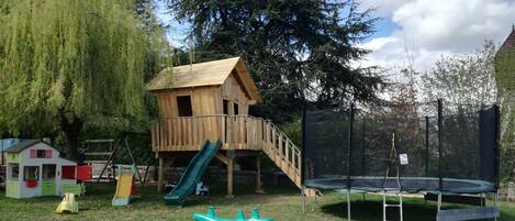 Une aire de jeux avec une cabane en bois, des toboggans, un trampoline et un petit bateau.
