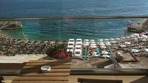 Eine Terrasse mit Blick auf das Meer und die Berge, Liegestühle und Sonnenschirme.