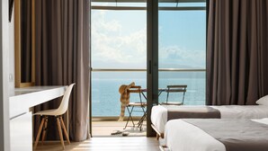 Ein Hotelzimmer mit großem Fenster, Schreibtisch, zwei Betten und einem Sessel.