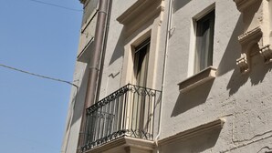 Ein Gebäude mit einem Balkon, der kunstvoll gestaltete Metallgeländer, einem großen vertikalen Rohr und zahlreichen Fenstern aufweist.