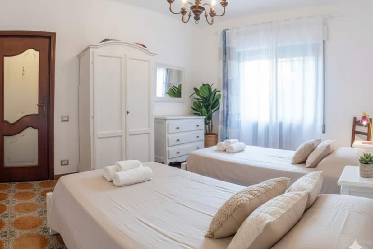 A hotel room with two beds, a wardrobe, a desk with a lamp, and a large window with curtains.