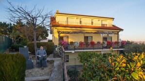 A two-story building with a balcony adorned with flowers, a wheelchair in the foreground, and a garden with various plants. - Agriturismo da Ernestina (Imperia)