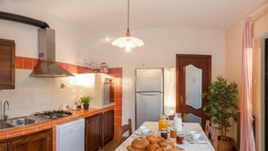 A kitchen with a gas stove, sink, and modern appliances. There is a dining table set with breakfast items. - Agriturismo da Ernestina (Imperia)