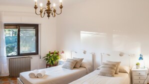 A bedroom with two beds, a chandelier, a window, and a radiator. - Agriturismo da Ernestina (Imperia)