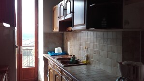 A kitchen with wooden cabinets, a tiled backsplash, and a window overlooking a balcony. - Auberge du coteau (Saint-Affrique)
