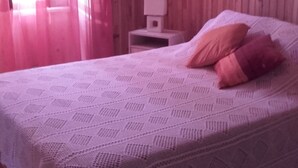 A bedroom with a wooden wall, a white bed with a patterned bedspread, and a nightstand with a lamp. - Auberge du coteau (Saint-Affrique)