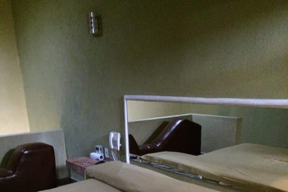 Quarto individual com uma cama de estrutura metálica, mesa de cabeceira com telefone e uma cadeira.